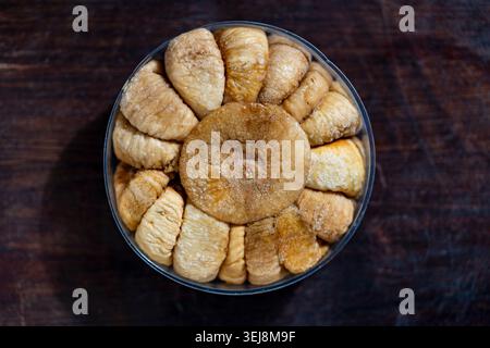Dried figs packed in circular pattern top view. Top view of sweet dried figs neatly arranged in a round plastic container on dark wooden background Stock Photo