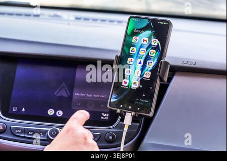 Augsburg, Germany - 25 May 2026: A close-up of a smartphone with Google apps mounted on an Opel car dashboard next to an Android Auto screen. Stock Photo