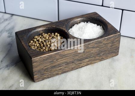Black oak salt and pepper pinch pot sitting on a marble countertop against a white, metro tile wall. Stock Photo