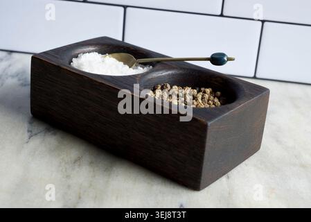 Black oak salt and pepper pinch pot sitting on a marble countertop against a white, metro tile wall. Stock Photo