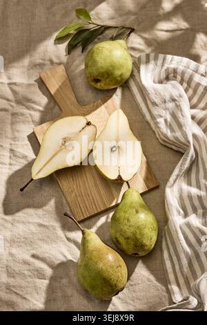 Overhead flat lay shot of fresh organic green pears, with two whole pears and one pear cut in half, arranged on a rustic wooden cutting board with a h Stock Photo