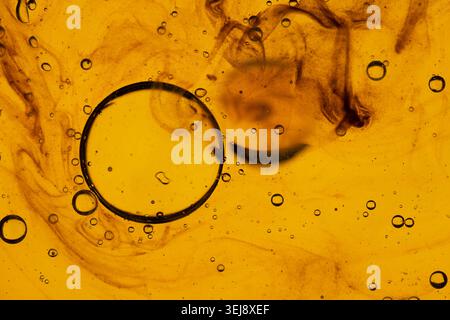 Macro shot of textured amber liquid with floating oil droplets and swirling dark ink patterns Stock Photo
