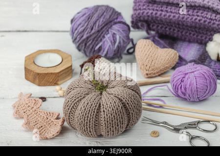 Handmade craft concept. Knitted pumpkin, crochet mushroom, yarn balls, knitting needles, and wooden buttons on a rustic white wooden background, close Stock Photo