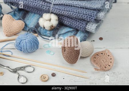 Handmade craft concept. Knitted pumpkin, crochet mushroom, yarn balls, knitting needles, and wooden buttons on a rustic white wooden background, close Stock Photo