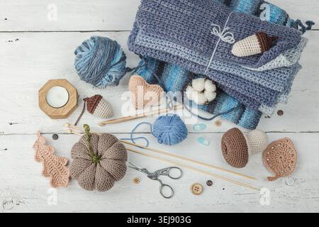 Handmade craft concept. Knitted pumpkin, crochet mushroom, yarn balls, knitting needles, and wooden buttons on a rustic white wooden background, top v Stock Photo