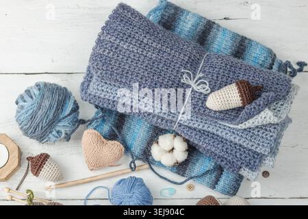 Handmade craft concept. Knitted pumpkin, crochet mushroom, yarn balls, knitting needles, and wooden buttons on a rustic white wooden background, top v Stock Photo