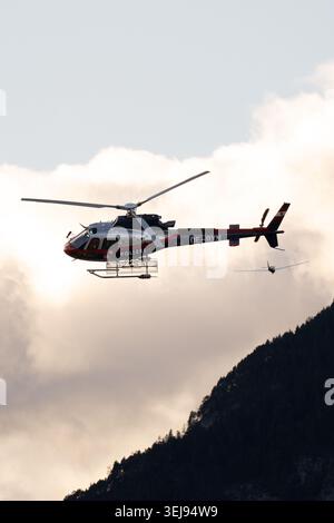 Austrian police helicopter OE-BXN flying over the Inn Valley near Innsbruck, Austria, with Alpine scenery and a motor glider in the background. Stock Photo