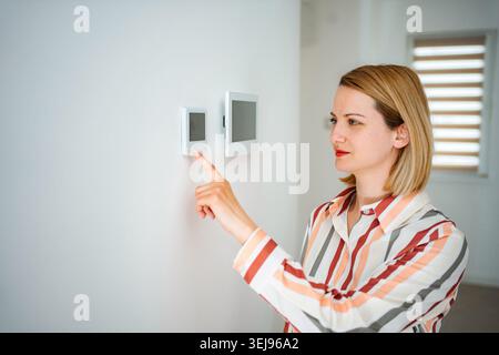 Woman adjusting smart thermostat controlling home climate Stock Photo