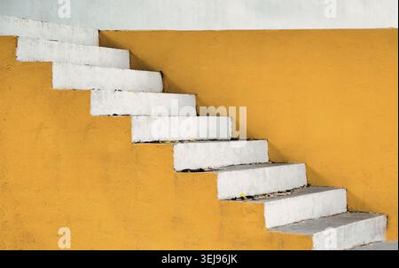 White outdoor staircase against a yellow wall, forming a minimalist geometric architectural detail with strong lines. Stock Photo