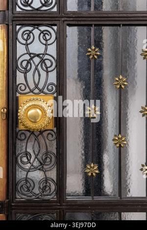 A decorative golden door handle mounted on an ornate wrought iron and glass door is attached to an entryway at a building exterior. Stock Photo