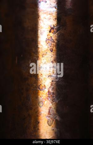 A close-up abstract shot of a textured copper metal surface showing signs of aging, patina, and dark rust spots. A sharp vertical beam of natural sunl Stock Photo