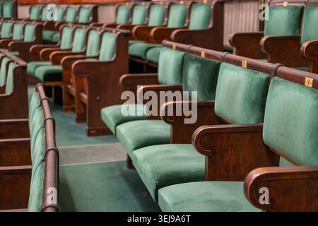 Empty wooden chairs with green velvet upholstery are arranged in rows at the Polish parliament. Stock Photo