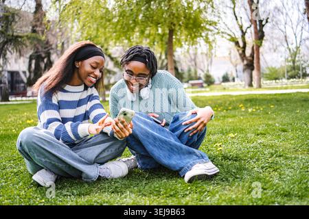 Young adult friends smiling using smartphone in park Stock Photo
