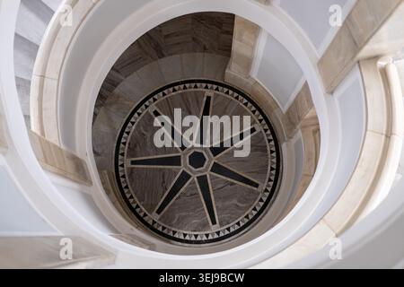 A circular staircase made of light marble is descending at a star-patterned floor building interior. Stock Photo