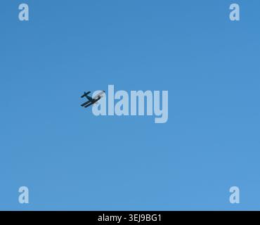 Small airplane flies against vast blue sky Stock Photo
