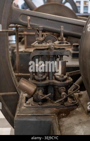 Mechanical speed governor is positioned near a large metal flywheel at an indoor industrial museum. Stock Photo