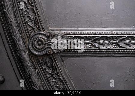 Ornate cast iron decorative architectural detail is mounted on a dark painted metal surface in an industrial environment. Stock Photo
