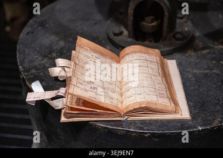 An antique ledger book containing handwritten financial records rests on a circular iron machinery base. Stock Photo