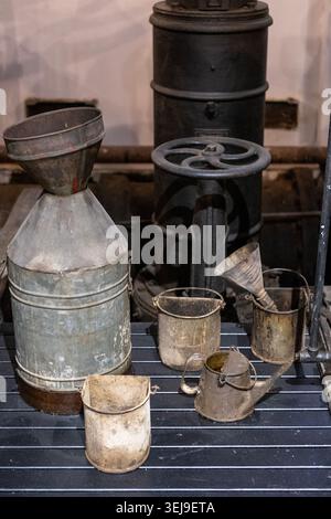 A collection of various vintage metal industrial funnels and containers sits on a slotted workbench in a workshop. Stock Photo