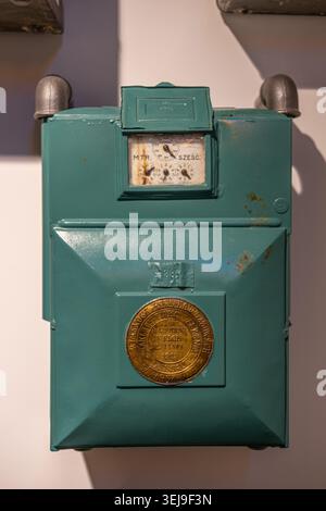 A vintage green rectangular gas meter with a dial and brass plaque from 1925 is mounted on a white wall. Stock Photo