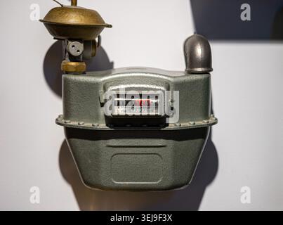 A grey mechanical gas meter with a brass top and numeric counter is mounted on an indoor wall. Stock Photo