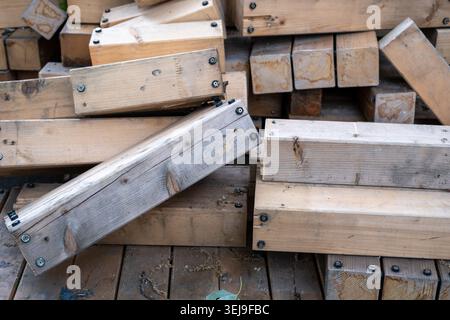Stacked rectangular wooden beams with metal screws in the ends are lying on a wooden deck outdoors. Stock Photo