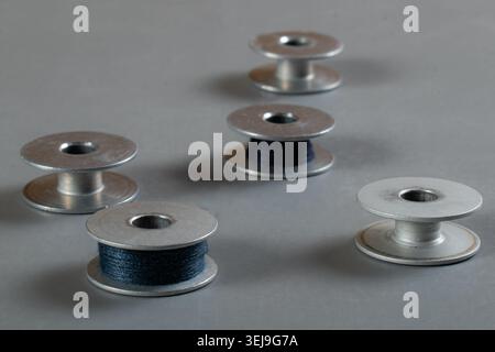 Metal sewing machine bobbins with dark thread arranged on a light background, showcasing essential tailoring and garment manufacturing accessories. Stock Photo