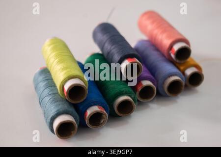 Colorful sewing thread spools arranged together on a white background, showcasing various thread colors used in textile, tailoring, embroidery and garment manufacturing. Stock Photo