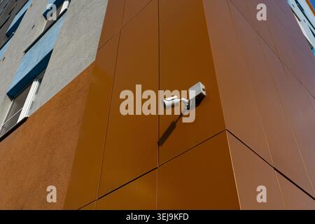 A Close-Up View of a Security Camera Mounted on a Modern Building Interior Wall with Textured Panels Reflecting Urban Architecture Stock Photo