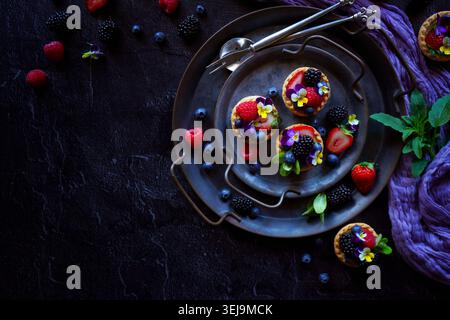 Lemon tarts with berries and viola edible flowers on dark background. Stock Photo