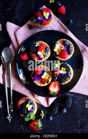 Lemon tarts with berries and viola edible flowers on dark background. Stock Photo
