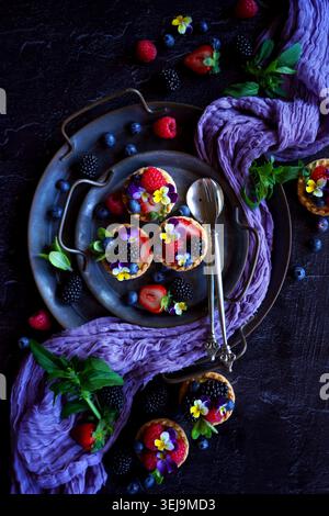 Lemon tarts with berries and viola edible flowers on dark background. Stock Photo