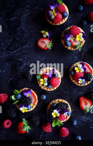 Lemon tarts with berries and viola edible flowers on dark background. Stock Photo