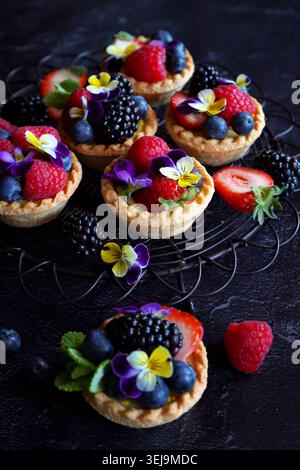 Lemon tarts with berries and viola edible flowers on dark background. Stock Photo