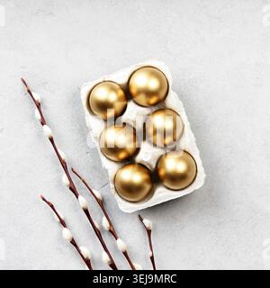 Luxury golden Easter eggs in carton with blooming willow branches on neutral stone background. Minimal spring holiday composition with copy space for Stock Photo