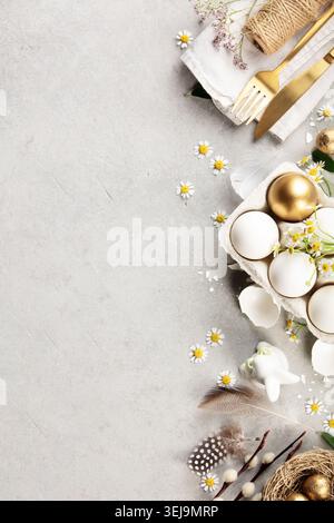 Stylish Easter flat lay with white and golden eggs in carton, chamomile flowers, bunny figurine, feathers and willow branches on light background with Stock Photo