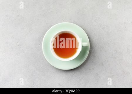 Top view of a cup of tea on a pastel mint saucer placed on a light gray textured background. Minimal composition with ample copy space, ideal for rela Stock Photo