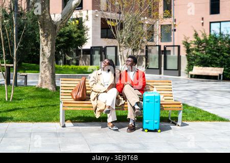 Cheerful curious african american couple man and woman travelers resting together on park bench. Stock Photo
