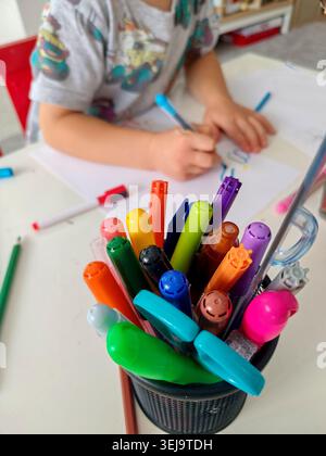 Boy learning to draw with colourful markers and pencils on white paper at home, creative childhood and early education concept. Stock Photo