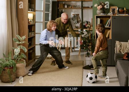 Senior Man Supervising Children Playing Soccer at Home Stock Photo