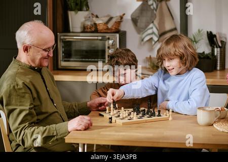 Senior Man Teaching Children Playing Chess at Home Stock Photo