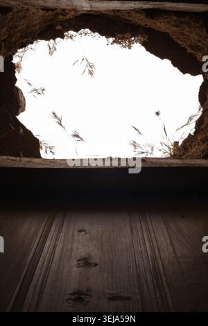 A vertically composed photograph captures an oval structural hole in a collapsed stone and compacted earth ceiling, through which an overcast sky and Stock Photo
