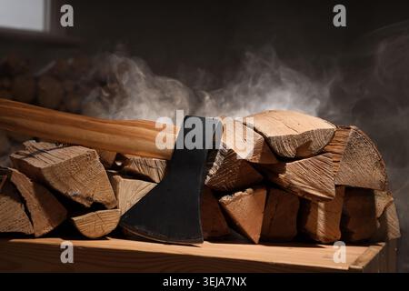 Sharp ax with firewood and smoke on table in dark carpenter's workshop Stock Photo
