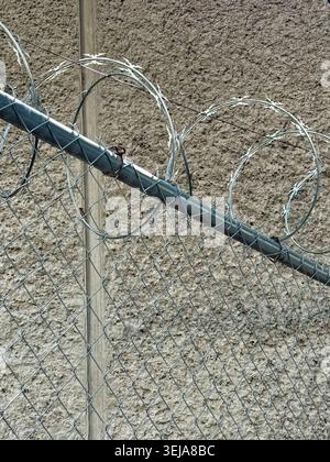 Razor wire on a chain-link fence against a rough concrete wall Stock Photo