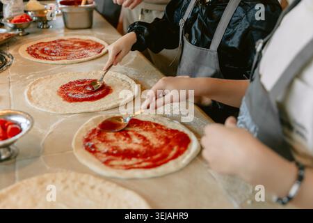 Chef preparing fresh pizzas in restaurant kitchen with tomato sauce Stock Photo