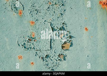 Weathered light blue paint peeling off an old metal plate with small rust spots. Abstract textured grunge background for urban and industrial design. Stock Photo
