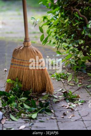 Close up of straw broom with yard waste on stone path Stock Photo