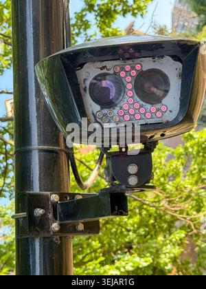 A ULEZ enforcement camera hangs displaced from its mounting on a lamp post in London, with purple sensor LED lights visibly active . Stock Photo