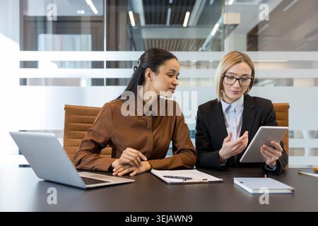 Two professional businesswomen collaborating in a modern office meeting, discussing projects and sharing insights while using a digital tablet for efficient teamwork and communication Stock Photo