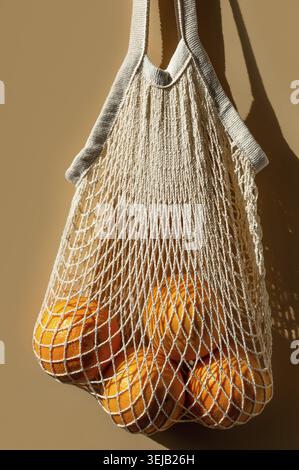 Ripe oranges in a white string bag. Beige background. Close up. Vertical crop Stock Photo